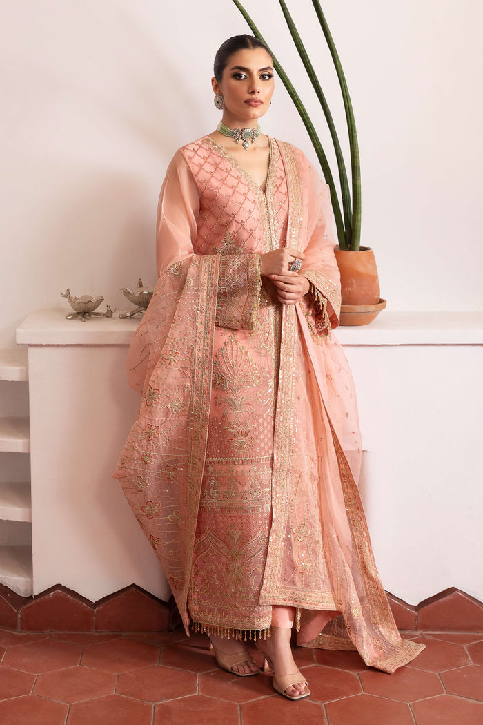 Model wearing full NAQSHI Muzna set: flamingo‑pink embroidered organza gown, straight PK‑silk trousers & heavily detailed dupatta styled for a cohesive look.
