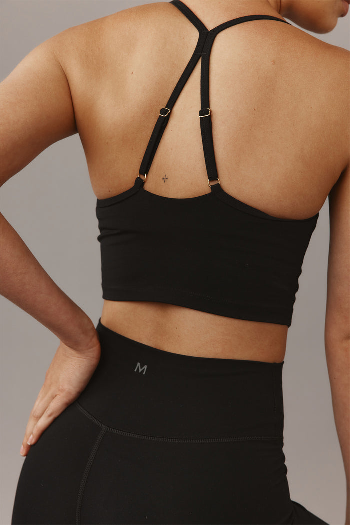 Back view of Olympic Tank in black showing adjustable strappy racerback and cropped fit on model with high-waist leggings showing M size mark