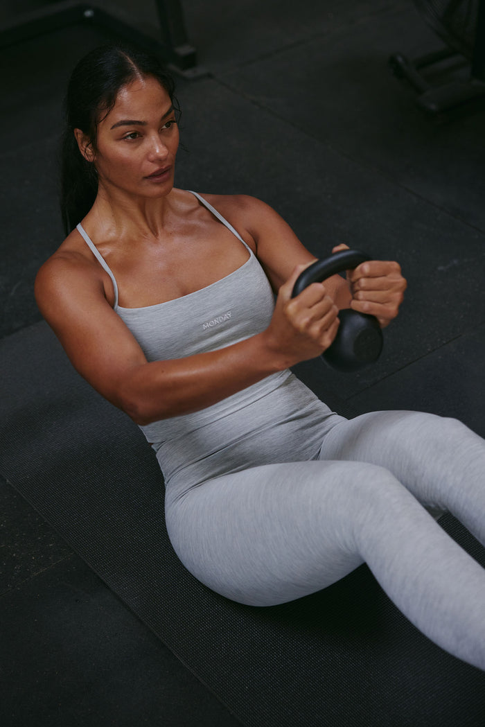 Angled view of Olympic Tank in Heather Grey on model showing scoop neckline, thin straps, MONDAY logo, fitted on black mat