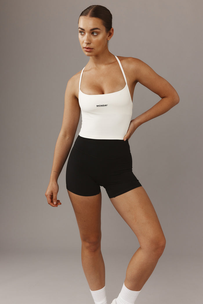 Front view of Olympic Tank in Ivory with scoop neckline, thin straps, cropped fit and center MONDAY logo on gray background