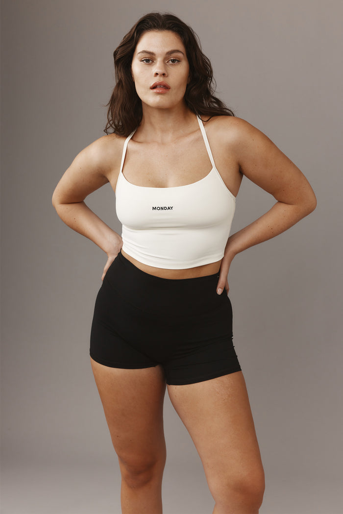 Front view of Olympic Tank in ivory showcasing cropped fit, thin straps, and center 'MONDAY' logo on gray background