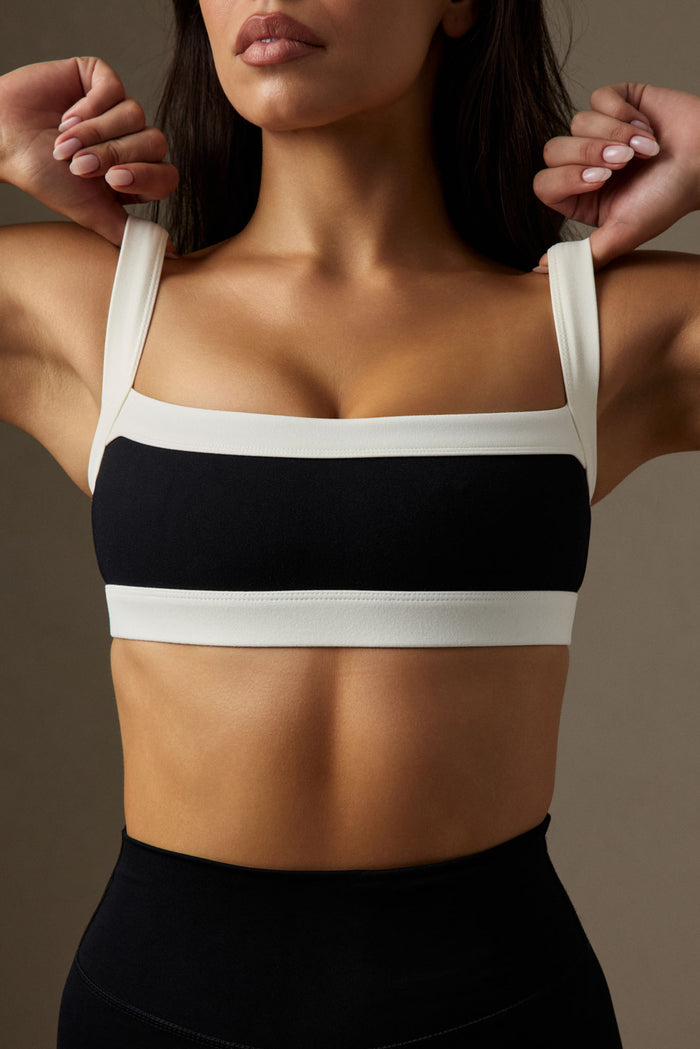 Close-up front view of Outpost Bra in black and ivory showcasing square neckline, color-block design, wide straps and cropped fit on a model with a neutral studio background