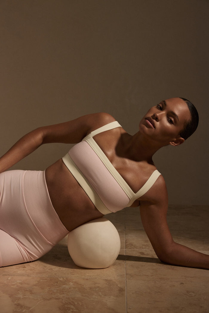 Angled view of Outpost Bra in heather powder pink and ivory on model, showing straight neckline, wide straps, and contrast trim