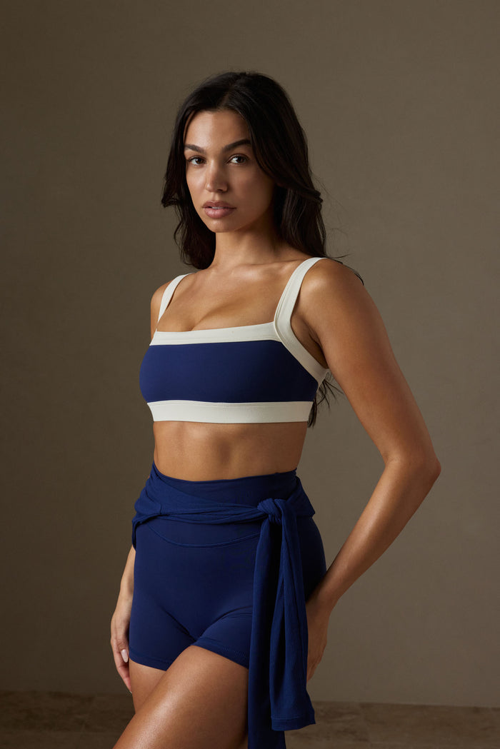 Three-quarter view of Outpost Bra in midnight with ivory trim, square neckline and wide straps on model against a neutral studio background