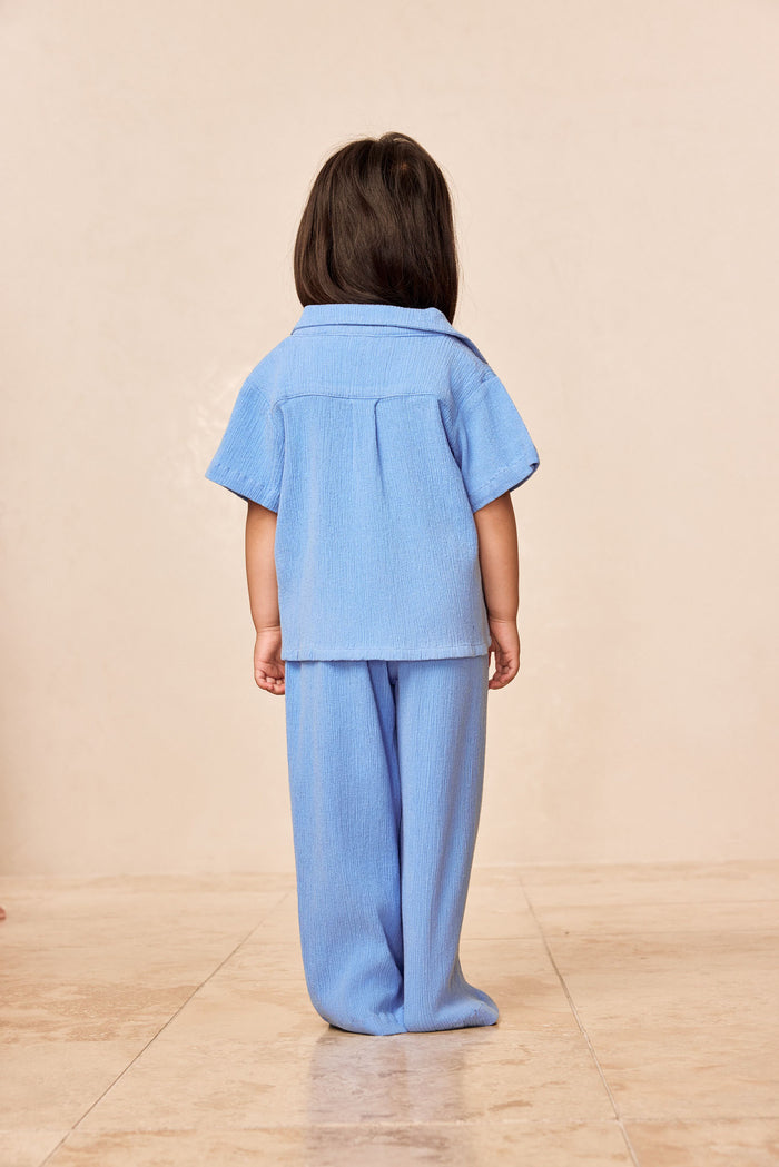Back view of Pacific Beach Shirt Kids in Azure Crinkle showing crinkle fabric, short sleeves and pleat on beige background