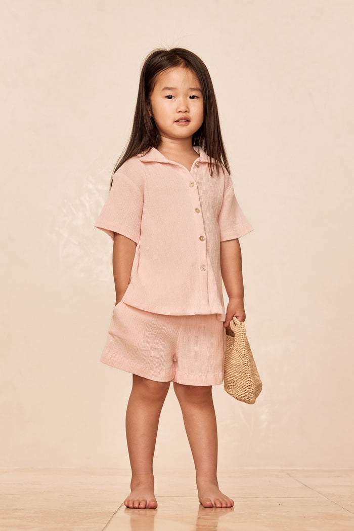 Front view of Pacific Beach Shirt Kids showcasing crinkled powder-pink fabric, short sleeves and button front against a neutral beige background