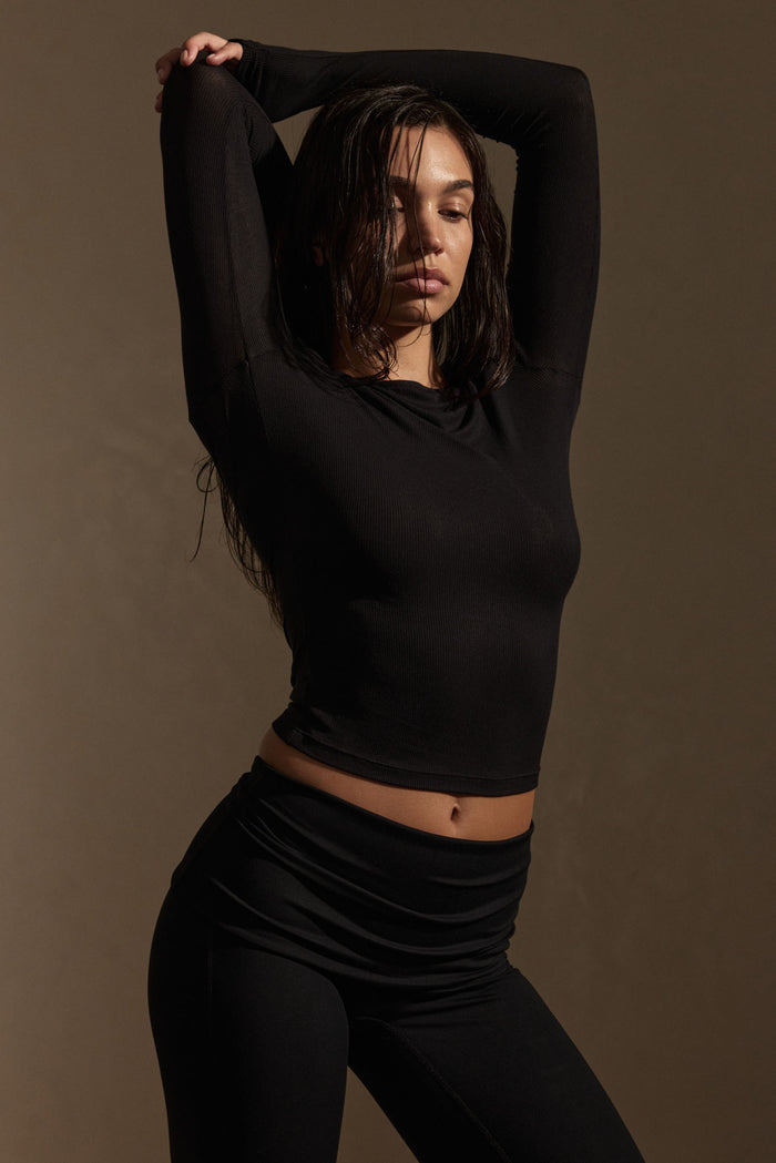 Three-quarter view of Paddington Long Sleeve in black lightweight rib showing fitted silhouette, long sleeves, and ribbed texture on model against a warm studio backdrop