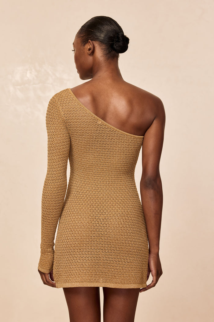Back view of Palermo Mini Dress, antique gold lace crochet, one-shoulder with single long sleeve on beige background
