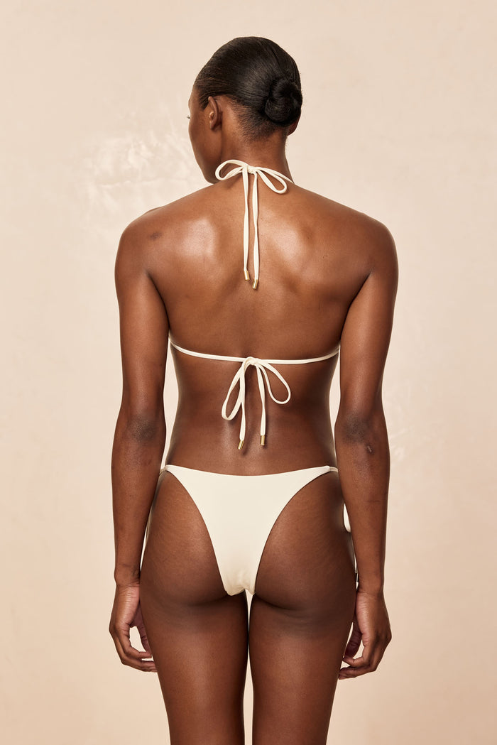 Rear view of Palma Bottom in ivory showcasing high-cut cheeky coverage and tie-side strings with gold tips against a neutral beige background