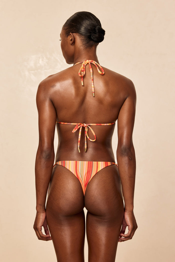 Rear view of Palma bikini bottom in Sardinia Stripe showing cheeky coverage and multicolor stripe pattern on beige background