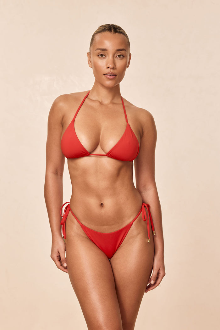 Front view of Palma Thong in Chili Pepper on model showing low-rise thong with side ties and gold-tipped ends