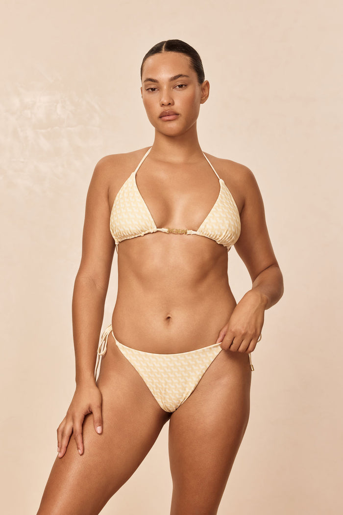 Front view of Monday Top in Ivory Geo on model, triangle halter with gold center hardware and adjustable ties, beige background