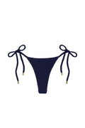 Front view of Palma Thong bikini bottom in midnight crinkle with textured fabric and side ties with gold tips on white