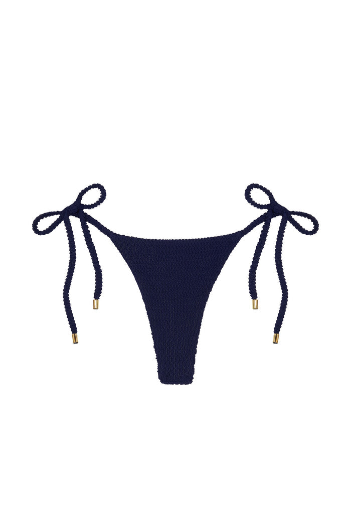 Front view of Palma Thong bikini bottom in midnight crinkle with textured fabric and side ties with gold tips on white