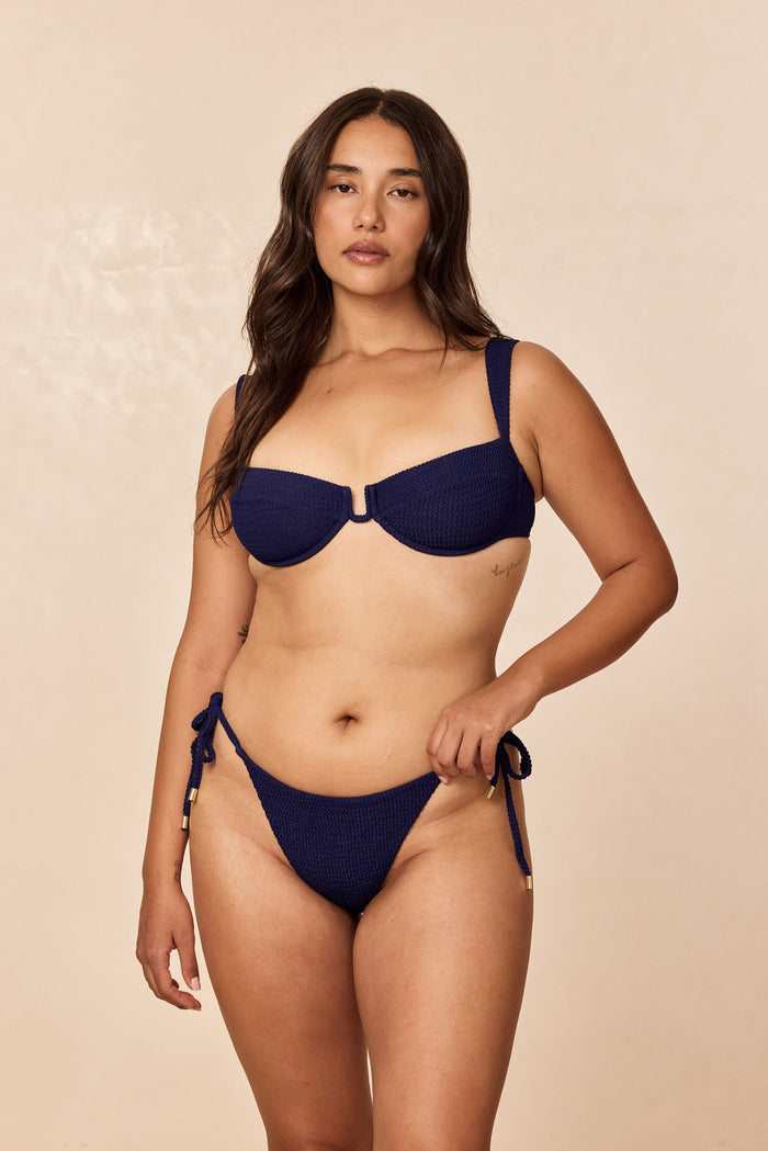 Front view of Palma Thong in Midnight Crinkle showing crinkle texture, side ties, and minimal coverage on a beige studio background