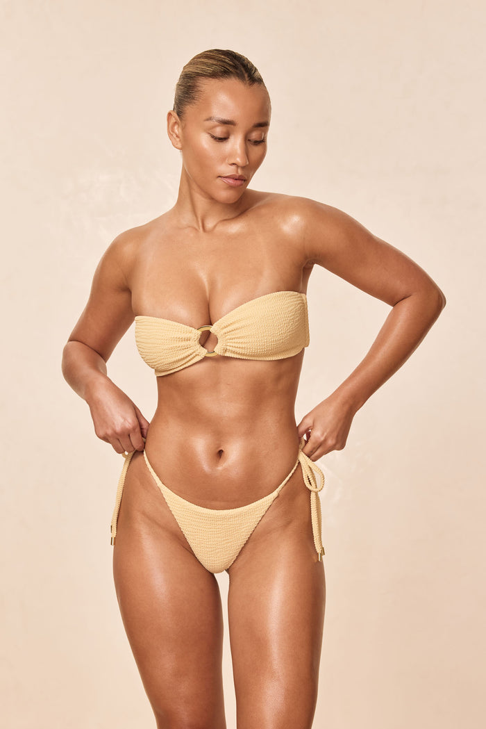 Front view of Palma Thong in raffia crinkle, high-cut tie-side thong worn by model against a neutral beige background