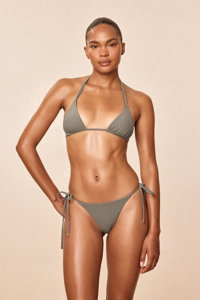 Front view of Palma Thong in Steel Lurex Rib on model showing ribbed texture and tie-side high-cut fit on beige background