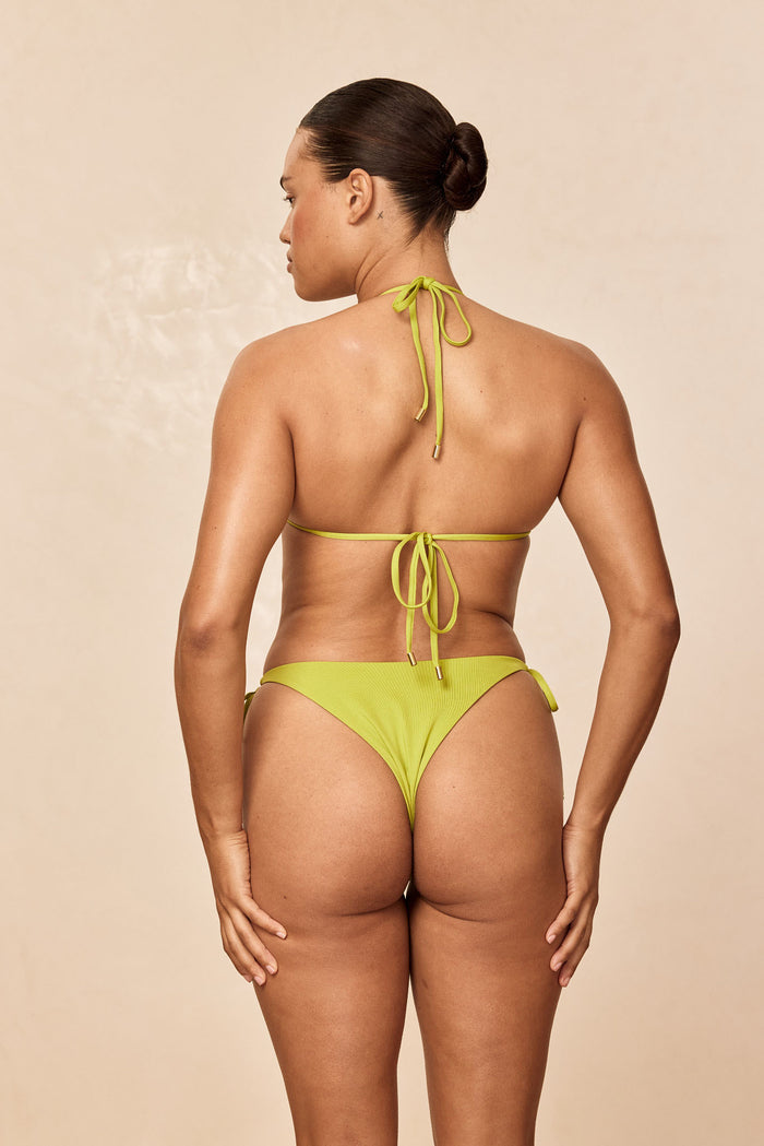 Back view of Palma Top in Apple showcasing thin adjustable neck and back tie closures on a model with a beige studio background