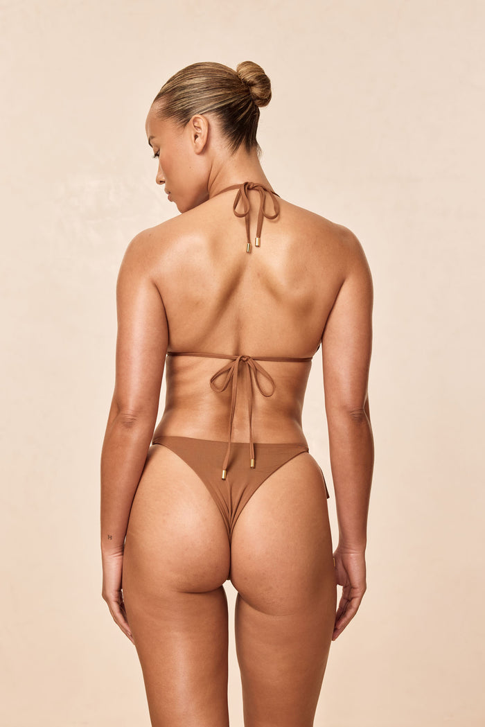 Rear view of Palma Top in Caramel showing halter tie-back straps with gold tips and low-back fit on model against a beige studio background