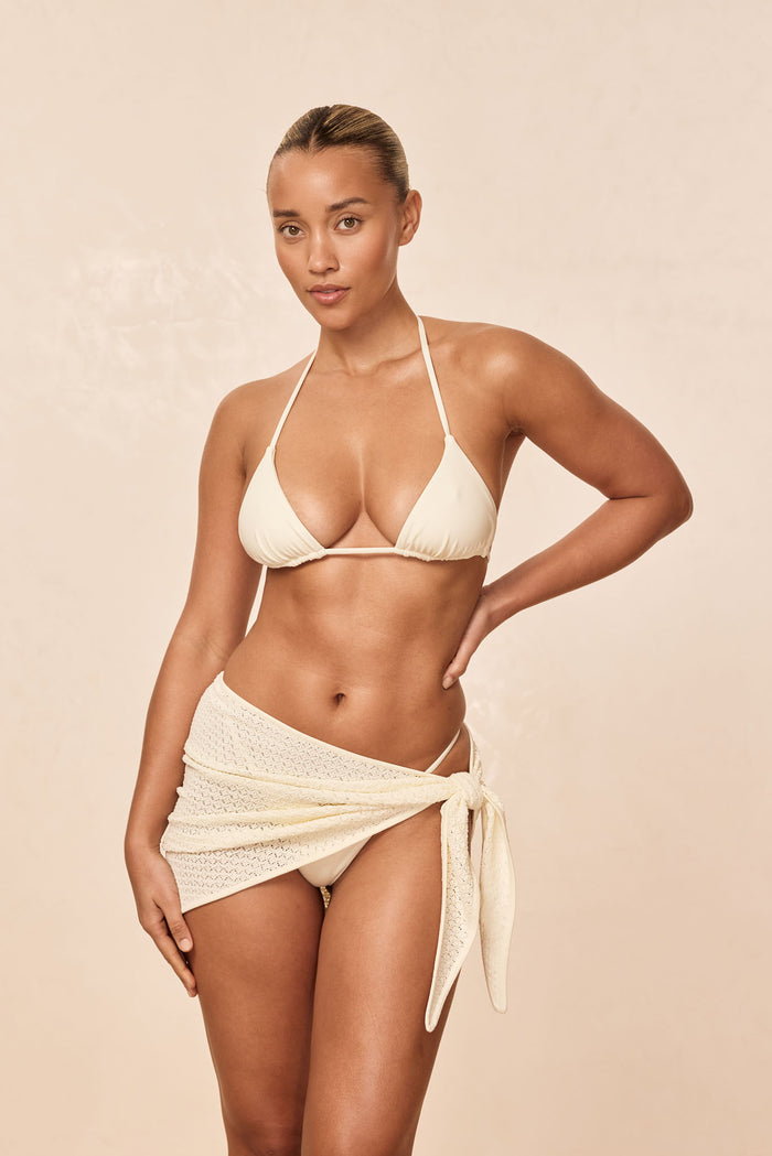 Front view of Palma top in ivory, halter triangle cups with thin adjustable neck and band ties on beige background