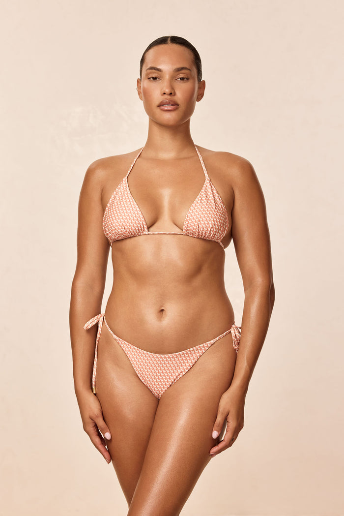 Front view of Palma Top (Micro Geo peach) on model, triangle halter cups with adjustable ties on a neutral background