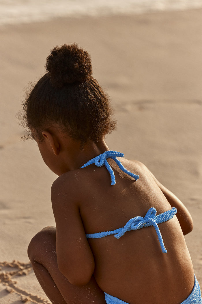 Back view of Palma Top and Seychelles Bottom set in azure crinkle showing rope-tie halter straps and tied back on sandy beach