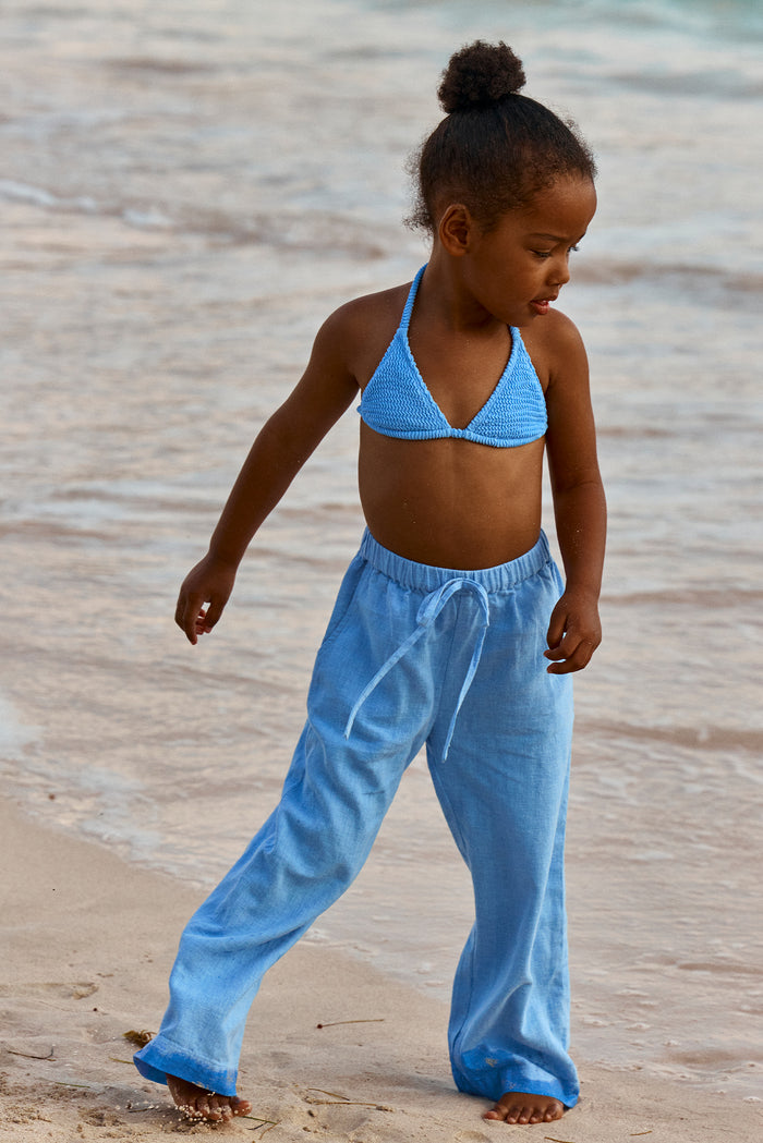 Child wearing azure crinkle halter bikini top and loose drawstring pants walking on a sandy beach