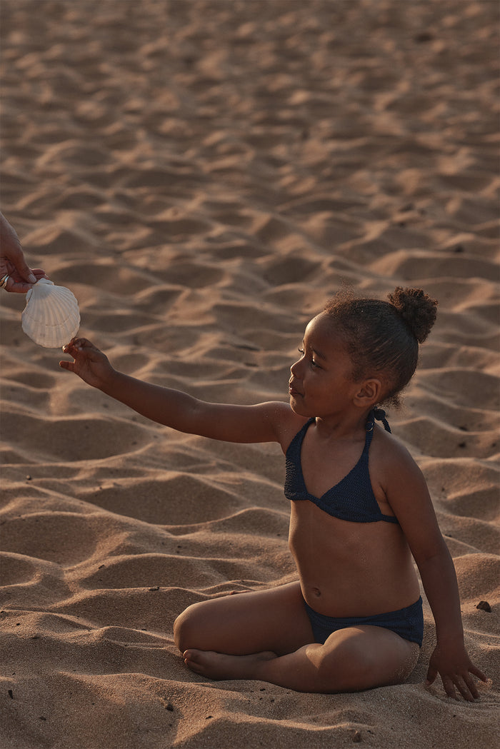 Child side view wearing Palma Top and Seychelles Bottom in Midnight Crinkle, showing crinkle texture and halter tie on sand