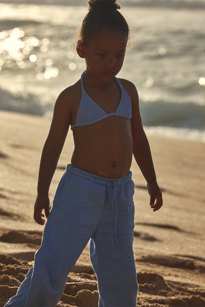 Front view of Tuscany Pant Kids in Pool blue on child model showing loose wide leg fit and drawstring waist on sunlit sandy beach
