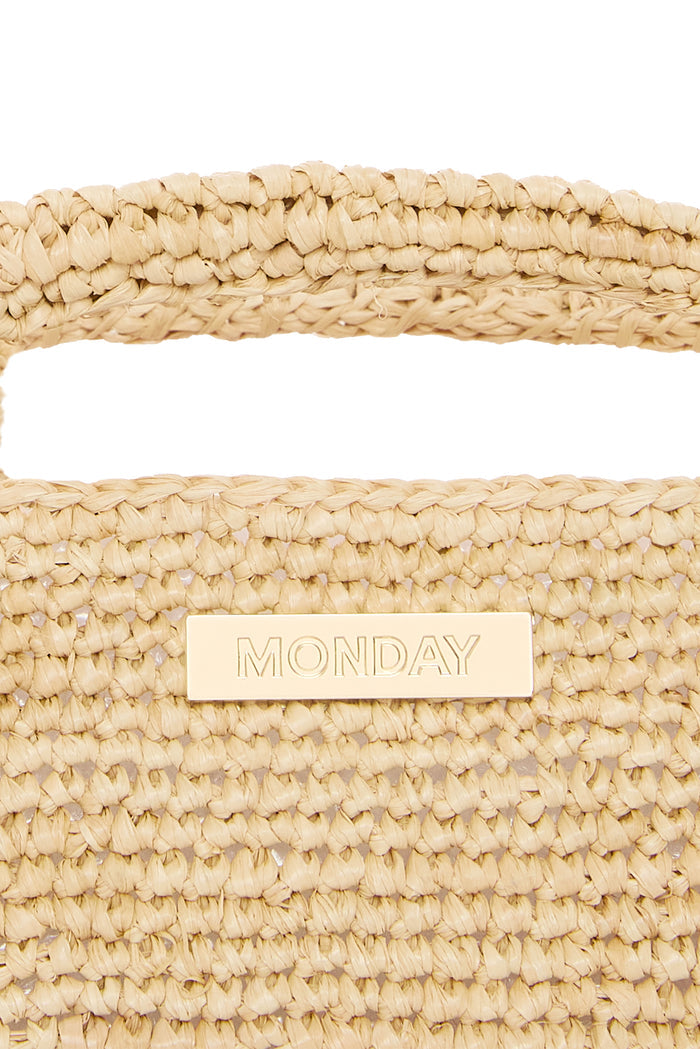 Close-up front of Paloma Mini Bag showing hand-crocheted natural straw texture, top handle, and gold plate engraved MONDAY on white background