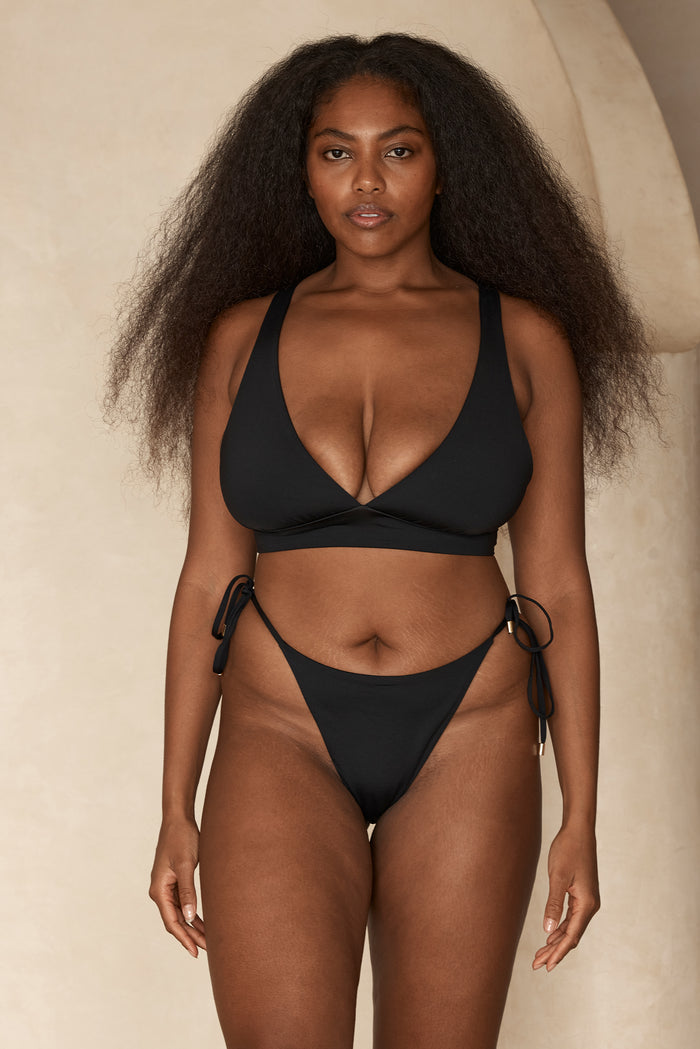 Front view of Palomino Bottom in black on model showcasing high-rise, high-leg cut and adjustable tie sides with neutral backdrop