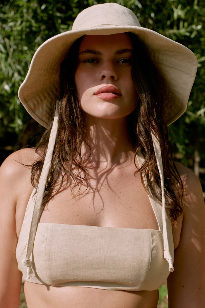Front close-up of Panarea Hat in natural showcasing wide floppy brim and long chin ties against sunlit leafy background