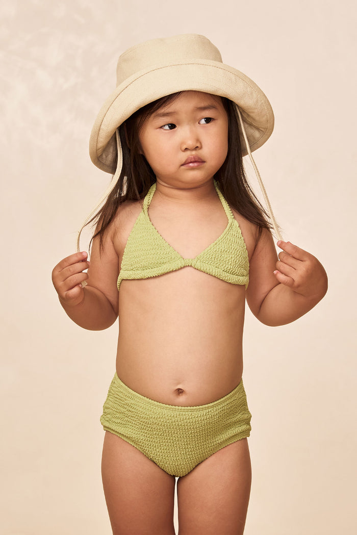 Front view of Panarea Mini Hat in natural canvas showing bucket silhouette and chin tie on child model against beige background