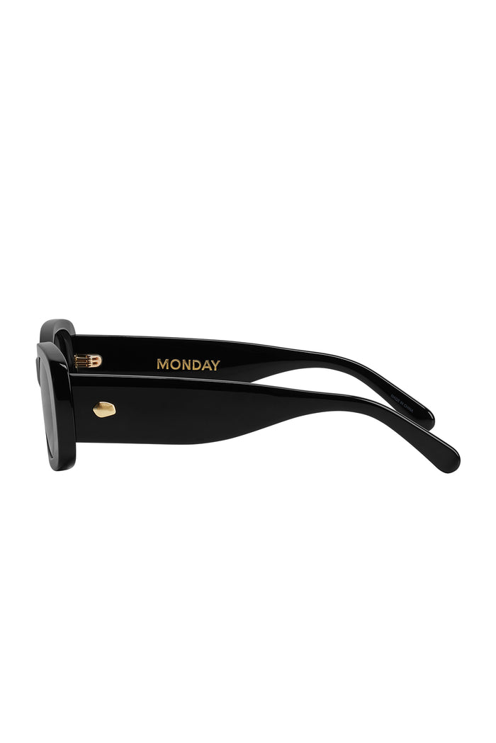 Side view of Piana sunglasses showing black acetate frame, square grey lenses, and gold MONDAY logo on white background