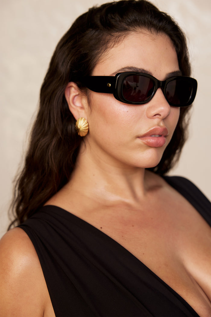 Three quarter close up of Piana sunglasses in black showing rectangular acetate frames and dark grey lenses on a neutral background