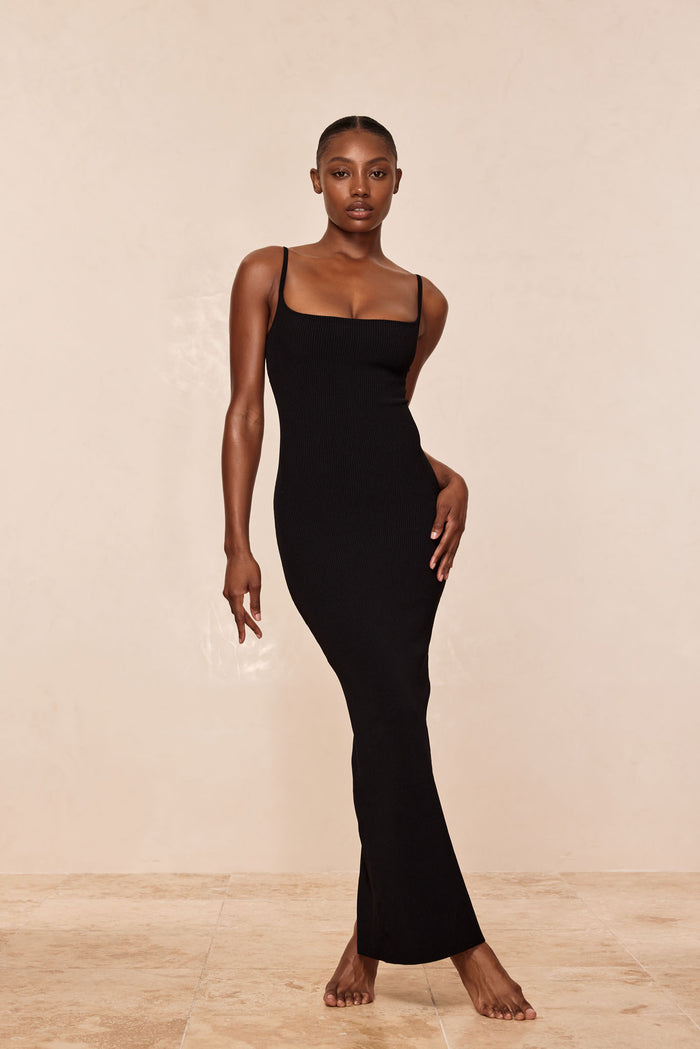 Front view of Provence Dress in black knit rib on model, slim bodycon fit with thin straps, beige studio background