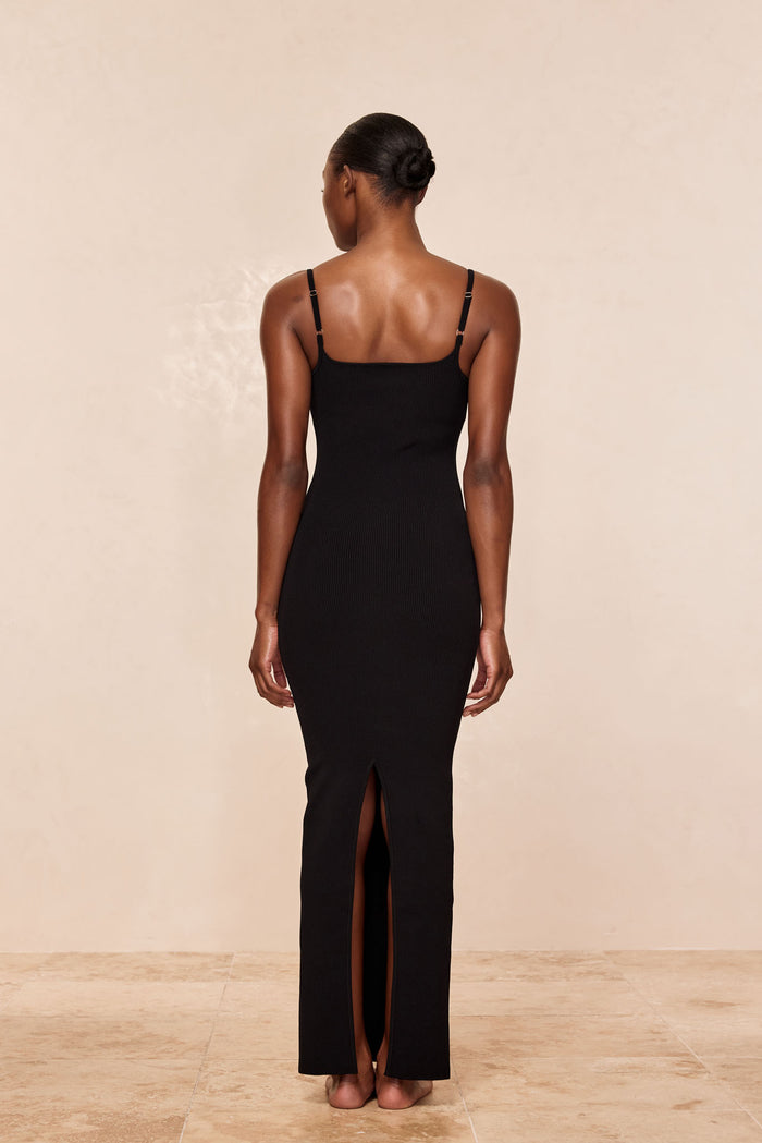 Back view of Provence dress in black knit rib with adjustable straps, fitted shape and back slit on beige background