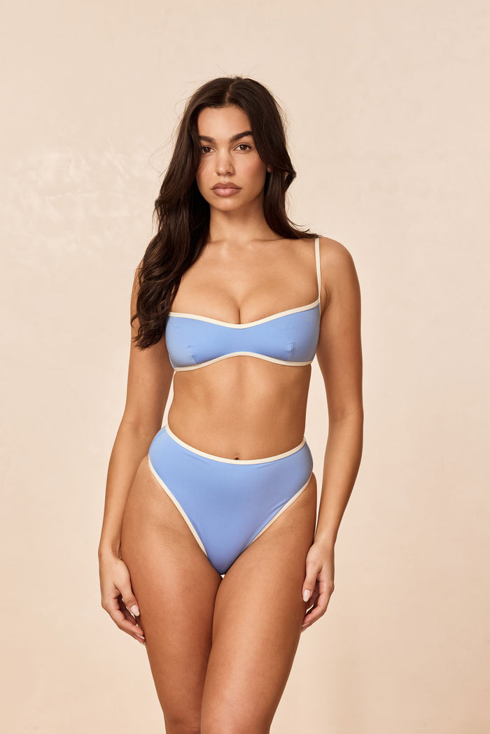 Front view of Ravello Bottom in Azure/Ivory, model showing high-waisted, high-leg cut and cheeky coverage on beige background