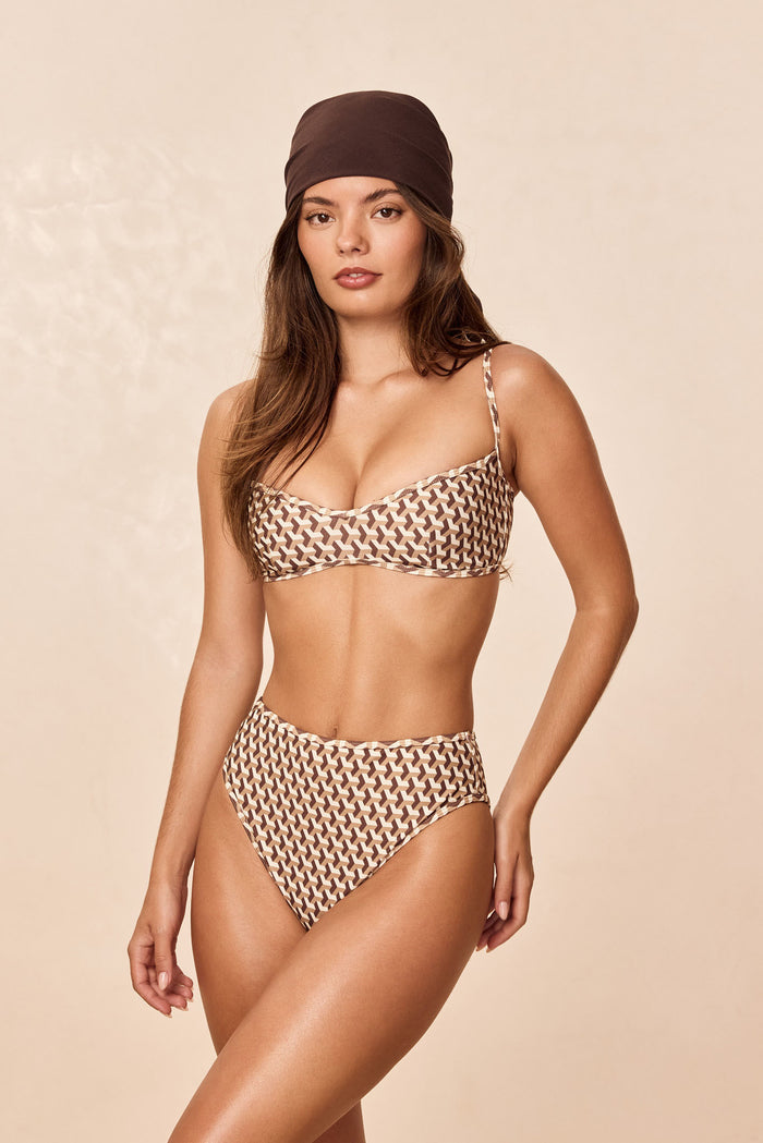 Three-quarter view of Ravello Bottom in Husk Geo showing high-waisted, high-leg, cheeky coverage on a model against a neutral beige background