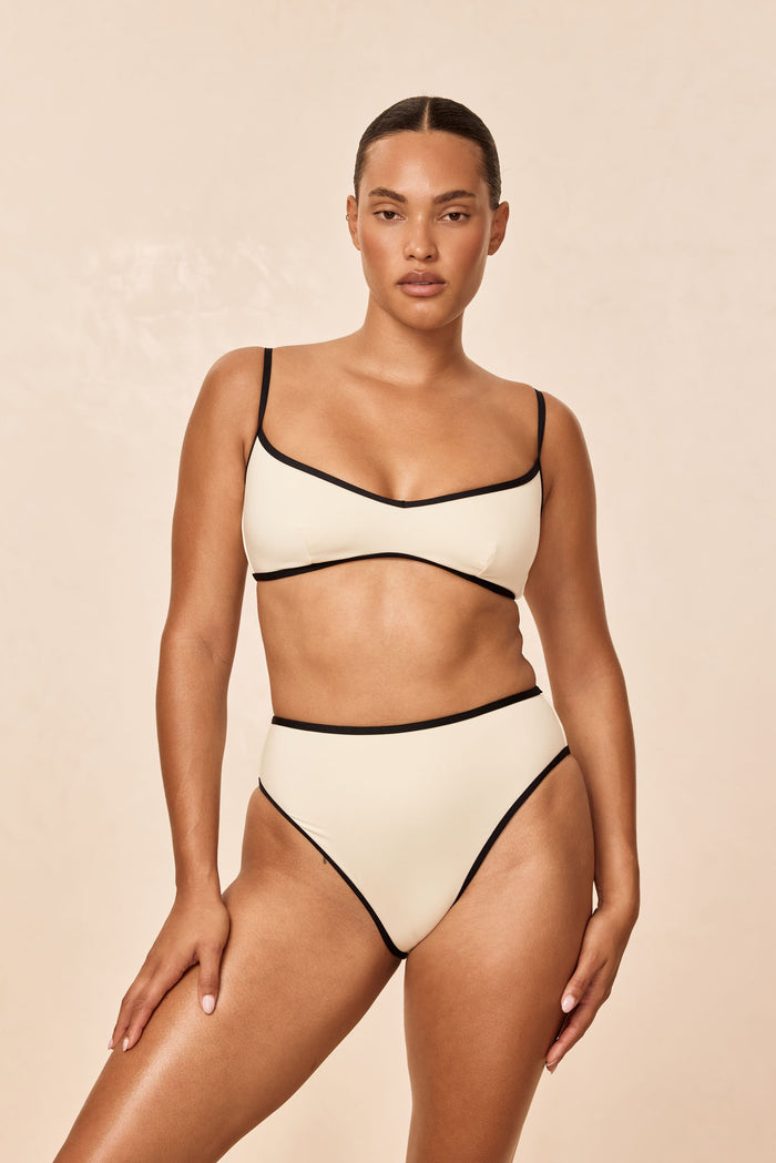 Front view of Ravello Bottom in ivory with black binding, high-waisted high-leg cheeky coverage, beige background