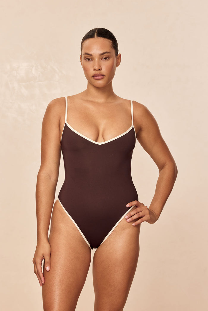 Front view of Ravello One Piece in espresso with ivory trim, V-neckline and adjustable straps on beige background