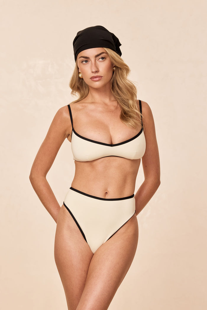 Front view of Ravello Top in ivory with black trim on model, scoop neckline and adjustable straps on beige background