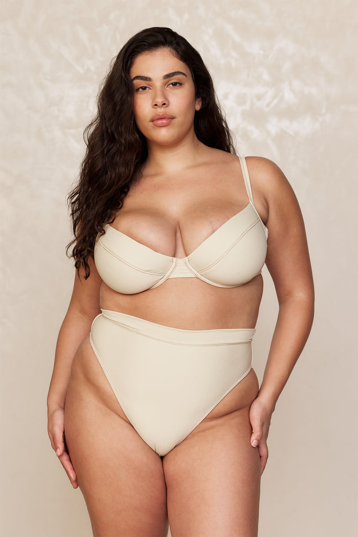 Front view of Riviera Bottom in Champagne Denim, high-waisted with high-cut leg and cheeky coverage on beige background