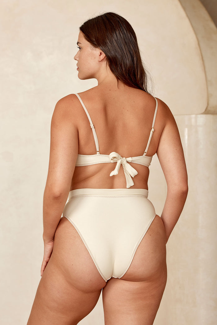 Back view of Riviera Bottom in Champagne Denim worn on model showcasing high-waist, high-cut leg and cheeky coverage