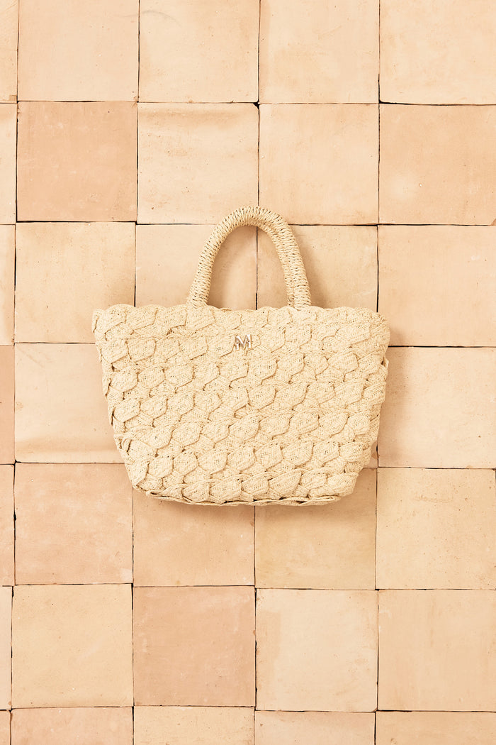 Front view of San Remo Mini woven straw tote with braided texture, wrapped handles and gold M monogram on tiled background
