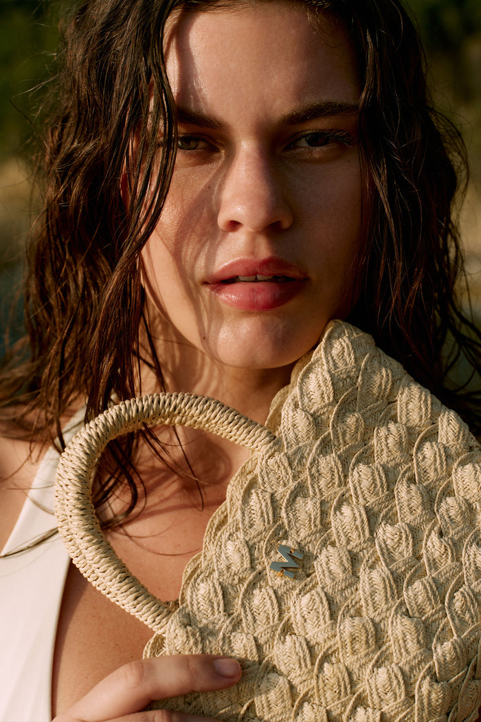 Close-up of San Remo Mini woven straw tote showcasing braided handles and gold M monogram held by model