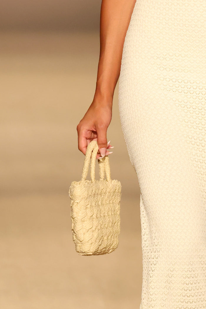 Close-up of San Remo Bag - Mini showing textured raffia, braided handles and gold M logo held by model against a neutral runway background