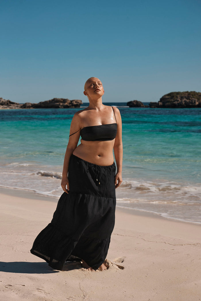 Front view of San Sebastian skirt in black showcasing tiered maxi silhouette and drawstring waist on a sunlit beach