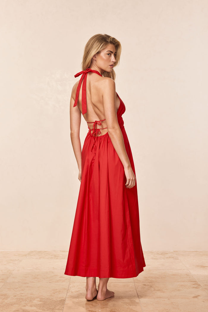 Rear three-quarter view of Santa Cruz Dress in Chili Pepper showing plunging halter open back with tie closures and ankle-length skirt on beige studio background