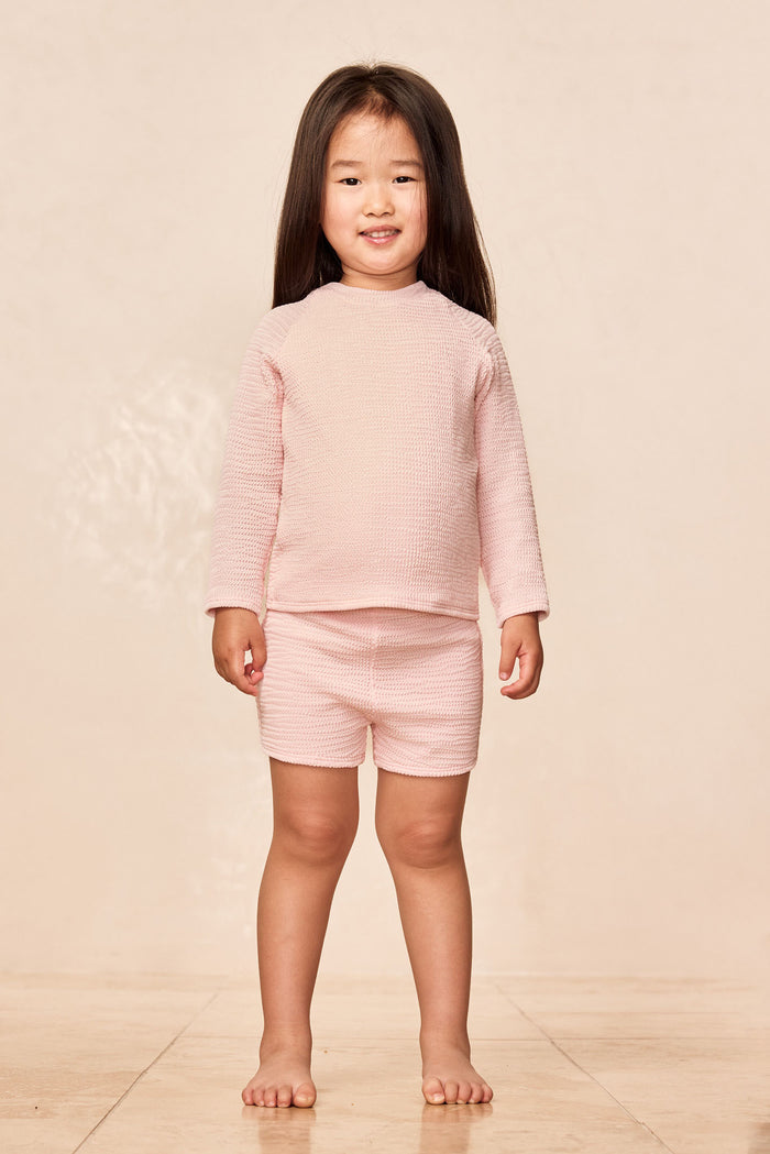 Front view of Santa Cruz kids shorts in Powder Pink Crinkle on a child model, textured crinkle fabric and elastic waist on beige background